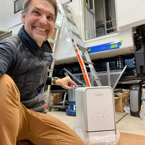 Man sitting on the floor next to a ladder and electronic device labeled 'Loch' in an indoor setting.